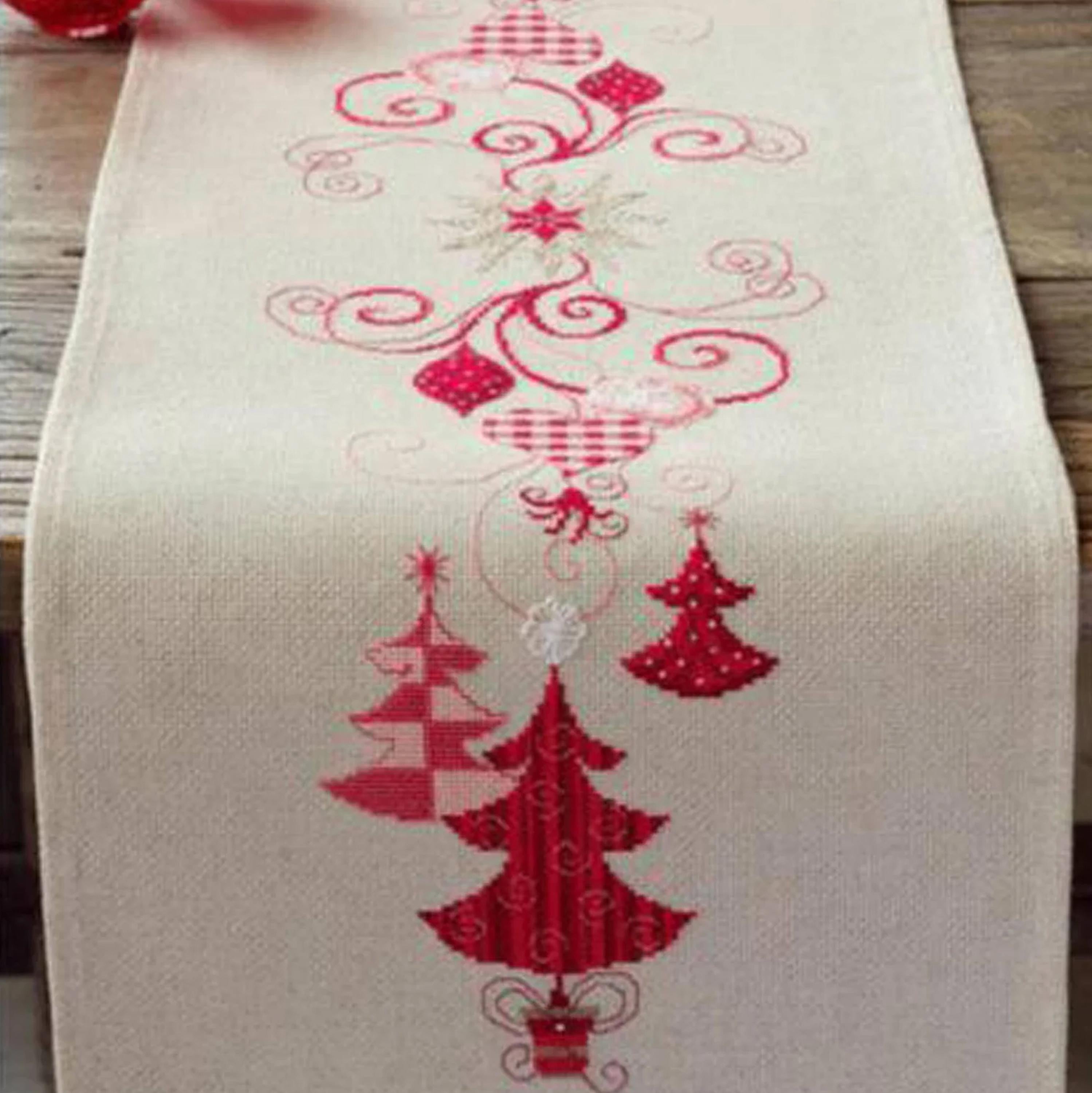 a table runner with a Christmas tree design, including red and white trees, ornaments, and a star.